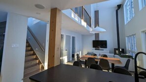 A modern kitchen with a dining area, a staircase, and a TV mounted on the wall. - Au Chalet Calme (Lac-Superieur)