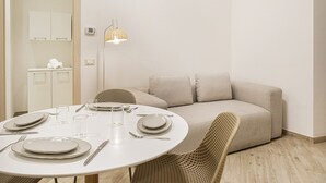 Un'area pranzo moderna con un tavolo rotondo apparecchiato per quattro persone, un divano e una sedia in vimini.