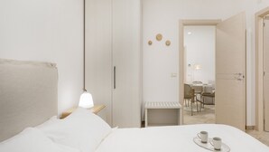 Una camera d'albergo minimalista con un letto, un comodino e una piccola zona relax.