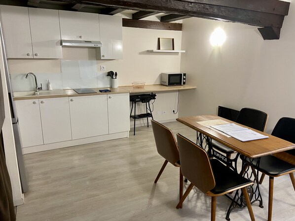A compact kitchen with white cabinets, a microwave, and a dining area with a table and chairs.