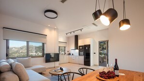 Una sala de estar moderna con un sofá, una mesa de centro y un televisor. Hay una zona de comedor con una mesa y sillas de madera, y una cocina con nevera y horno.