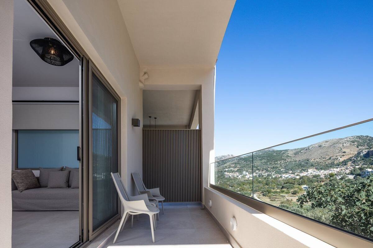 Un balcon avec un canapé et des fauteuils, une vue sur un paysage vallonné et un aménagement intérieur moderne.