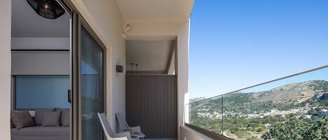 Ein Balkon mit einer Couch und Stühlen, Blick auf eine hügelige Landschaft, und ein modernes Interieur.