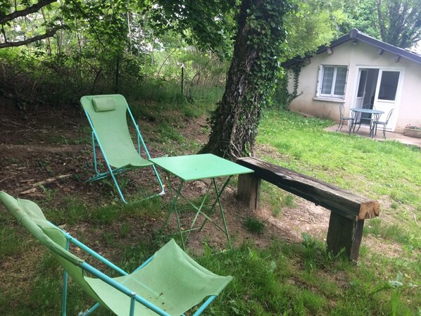 Una pequeña zona de estar al aire libre con un banco de madera y dos sillas verdes.