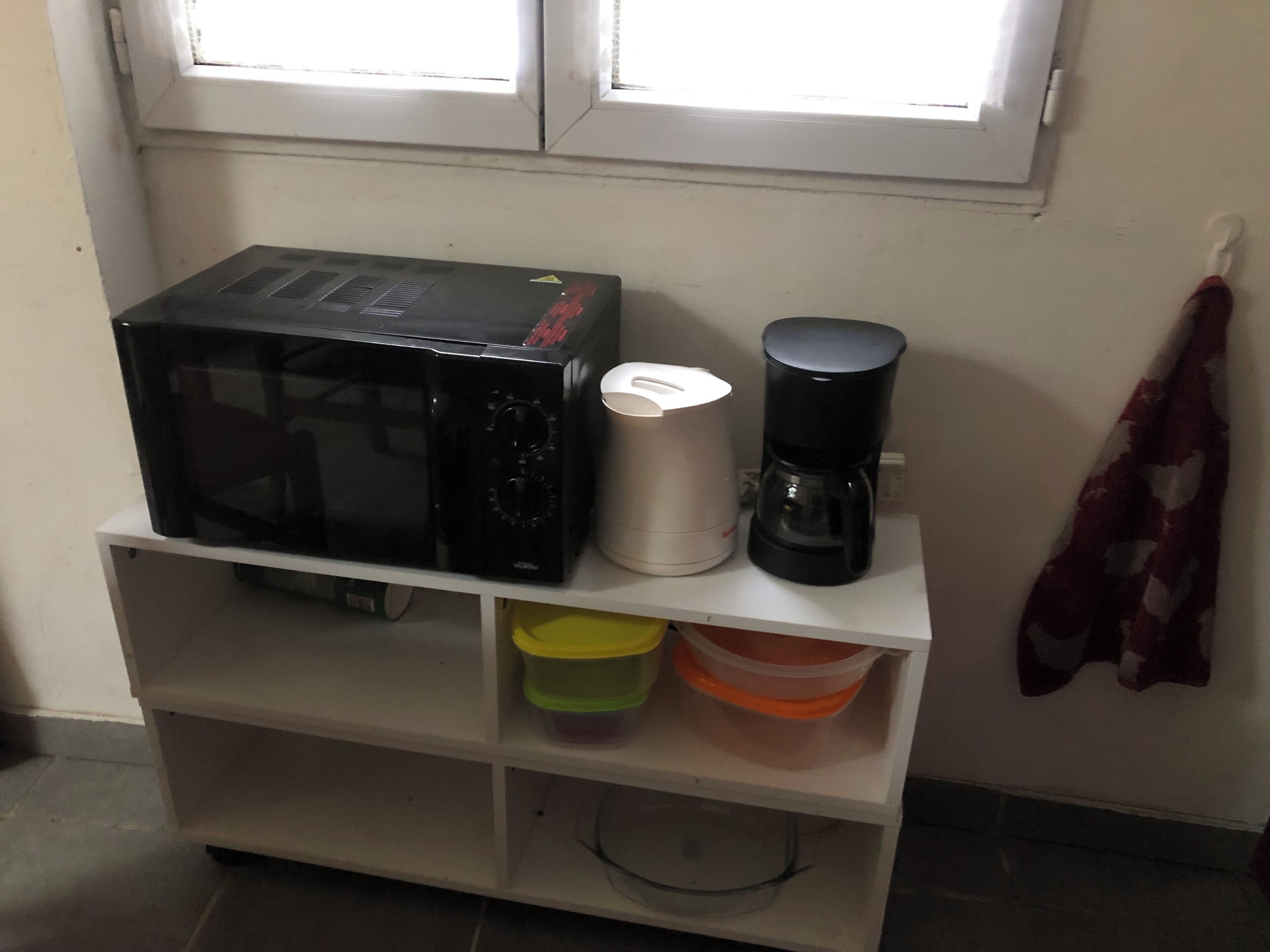 Un área de cocina con microondas, cafetera y recipientes de almacenamiento sobre un estante blanco.