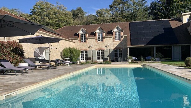 A swimming pool with lounge chairs and umbrellas, a building with solar panels, and a stone facade. - Domaine des Rives D'ormoy : Athamante (Ormoy-la-Rivière)