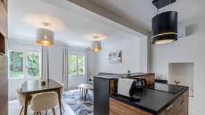 A modern kitchen with a central island, pendant lights, and a dining area with a table and chairs. - Domaine des Rives D'ormoy : Athamante (Ormoy-la-Rivière)
