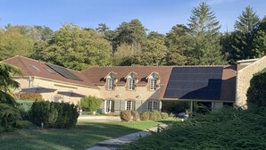 A large house with a stone facade, multiple chimneys, and a sloped roof with solar panels. - Domaine des Rives D'ormoy : Athamante (Ormoy-la-Rivière)