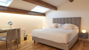 A bedroom with a bed, bedside table, lamp, desk, chair, and a skylight.