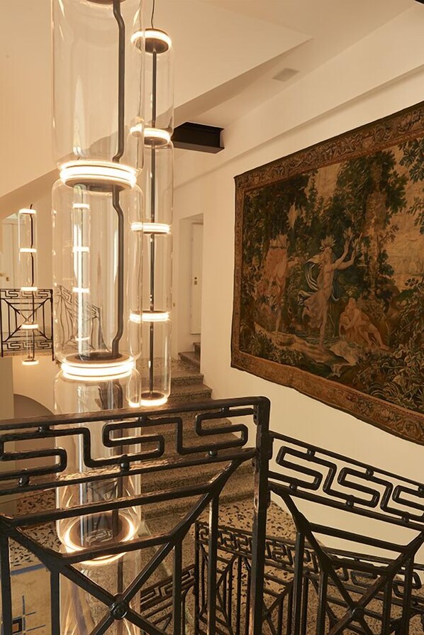 A staircase with a black metal railing and a large tapestry on the wall. - Palazzo Greco Stella (Lamezia Terme)