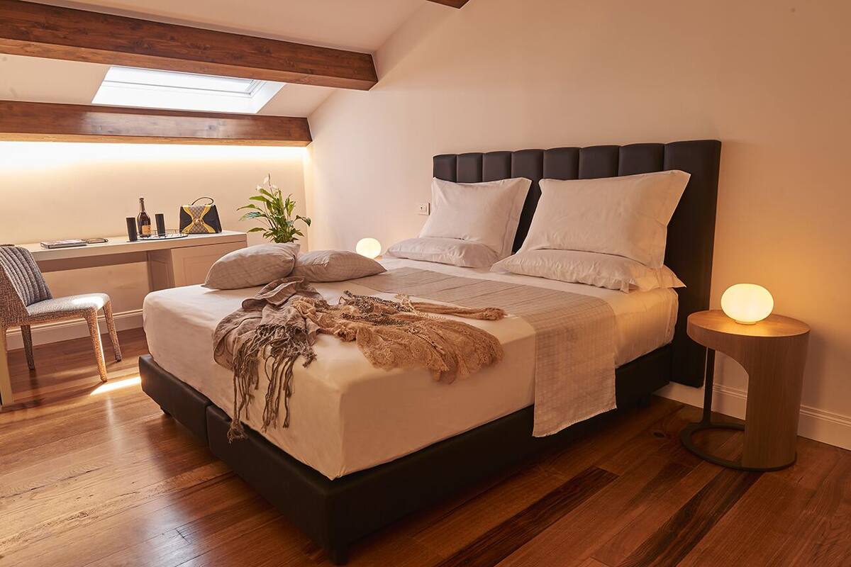 A bedroom with a large bed, wooden flooring, a desk with a chair, and a skylight.