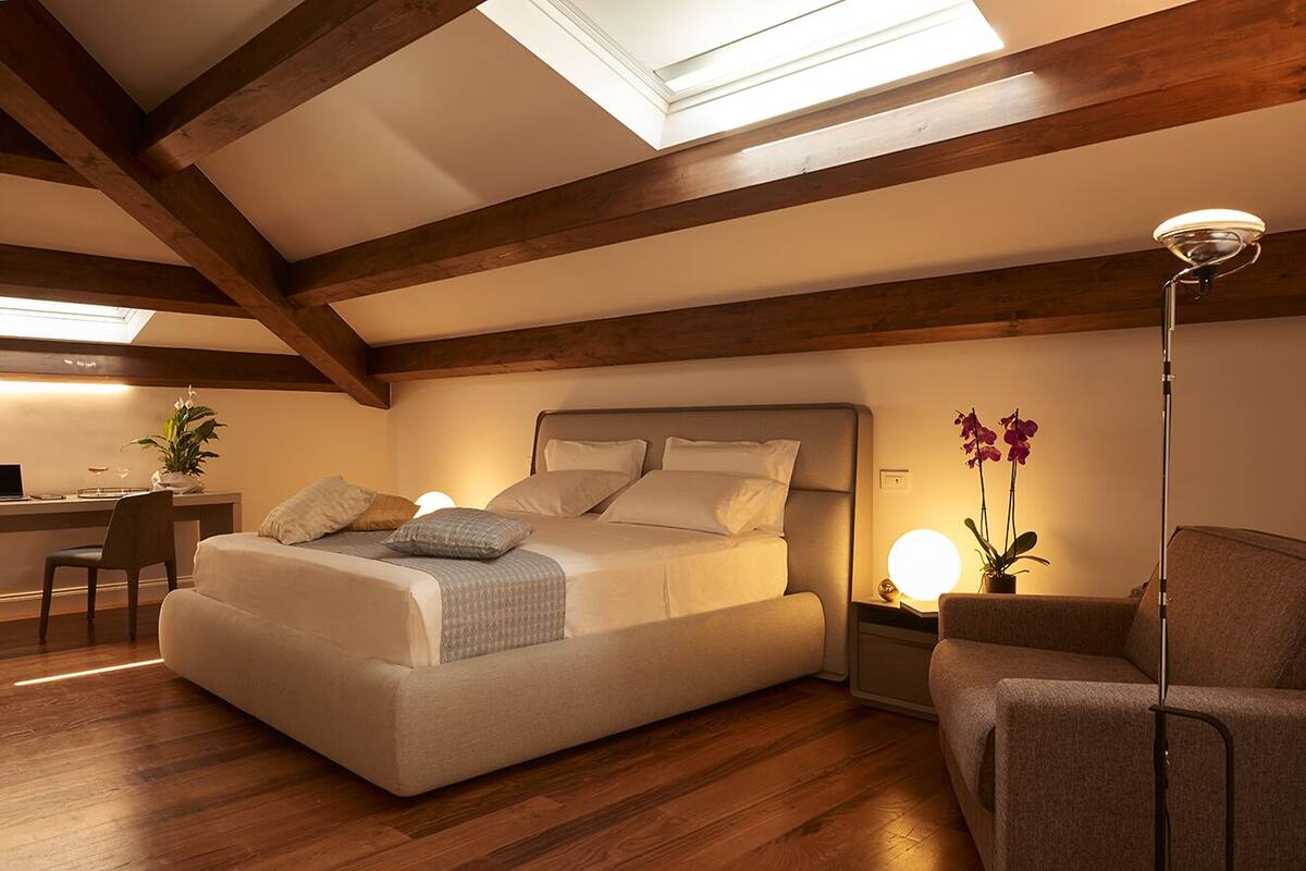 A bedroom with a bed, a desk, a chair, a sofa, and a floor lamp.