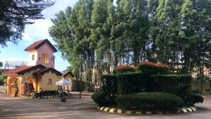 Un edificio con tetto rosso e facciata gialla, immerso in un giardino curato con siepi ordinate e alberi alti.