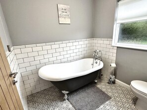 Un baño con una bañera independiente, paredes con azulejos blancos y una alfombra estampada en el suelo.