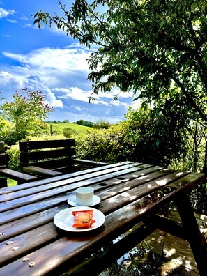 A wooden picnic table with a cup and a packet of snacks. - Renovated Cottage in Sherborne With Stunning Views (Sherborne)