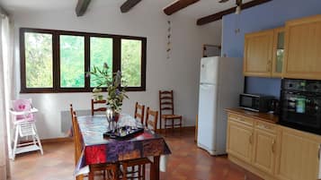 A dining area with a table set for four, a refrigerator, wooden cabinets, and a window with a view of greenery.