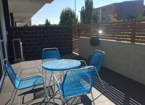An outdoor patio with a round table and four blue chairs, a brick wall, and a wooden fence.
