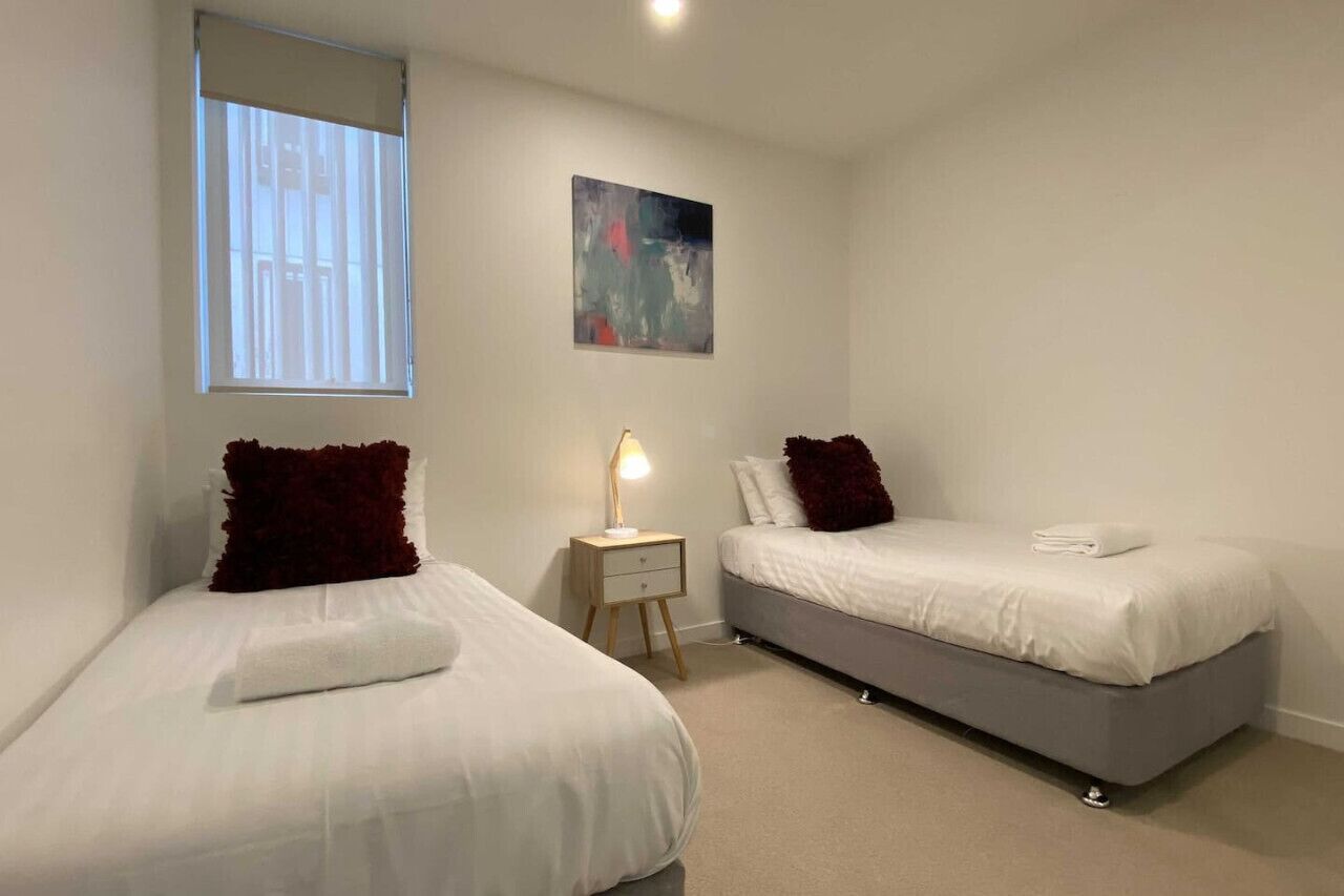 Une chambre avec deux lits, une table de chevet, une lampe, une fenêtre et un tableau au mur.