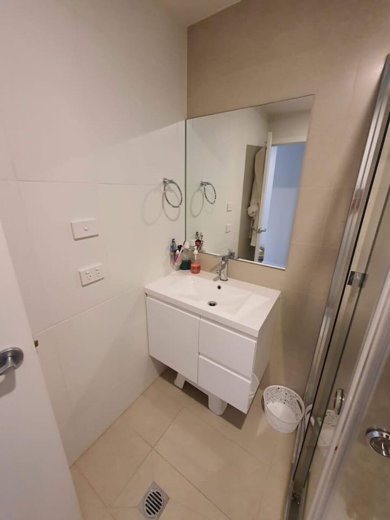 A small, modern bathroom with a white vanity, a mirror, and a shower area.