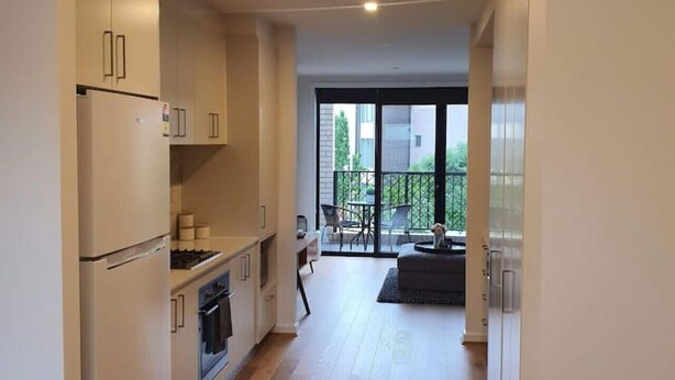 Una cucina moderna con mobili bianchi, un frigorifero e un fornello. C'è un'area pranzo con tavolo e sedie, e vista all'esterno attraverso ampie finestre.