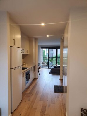 A modern kitchen with white cabinets, a refrigerator, and a stove. There is a dining area with a table and chairs, and a view of the outside through large windows.