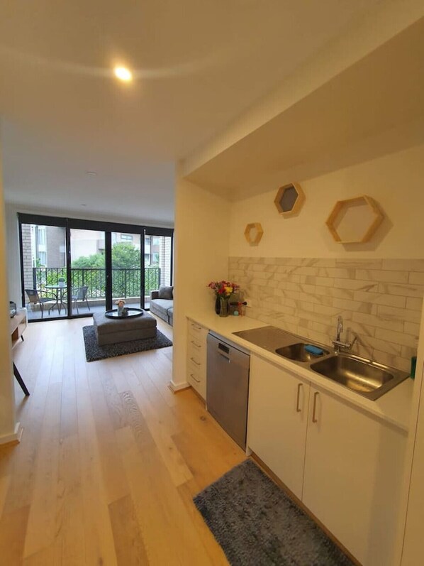 A modern kitchen with a dishwasher, a sink, and a dining area with a sofa and a table.