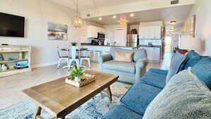A modern living room with a sofa set, a coffee table, and a dining area with chairs. - Gulf Views - Beach Chair Service - Zero Entry Pool + Hot Tub - Beach Resort 403 (Miramar Beach)