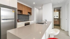 Une cuisine moderne dotée d’un réfrigérateur en acier inoxydable, d’un crédence en carreaux noirs, de meubles en bois et d’un grand îlot central avec un évier et des tabourets de bar.