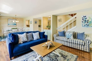 A living room with a blue sofa, a checkered sofa, a wooden coffee table, and a staircase.