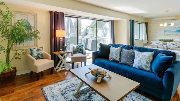 A living room with a blue sofa, a wooden coffee table, a chair, a lamp, and a large window. - Luxury Villa Golf Beach & Pool Access Hilton Head (Hilton Head Island)