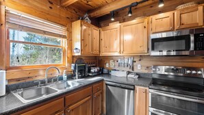 Una cocina con armarios de madera, electrodomésticos de acero inoxidable, lavavajillas y una ventana con persianas.