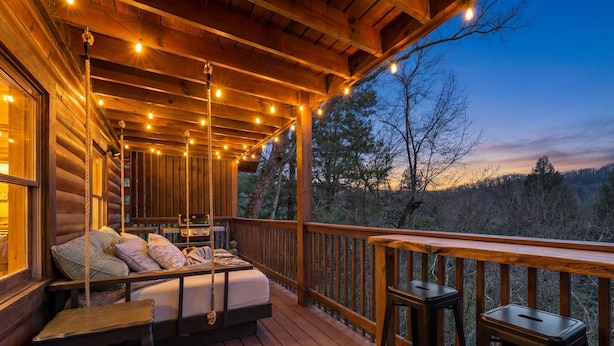 Una terraza de madera con una cama, taburetes y guirnaldas de luces.