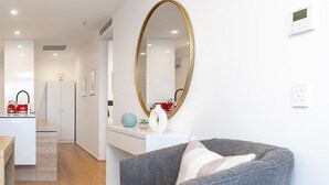 Una sala de estar moderna con un sofá gris, una consola blanca y un espejo grande con marco dorado.