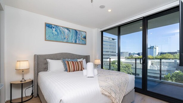 Un dormitorio moderno con una cama grande, vistas de la ciudad a través de ventanales y un cuadro en la pared.