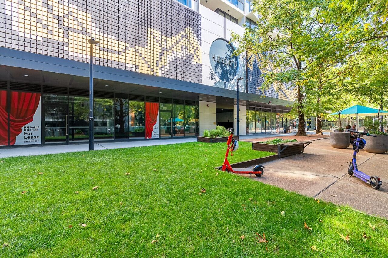 A modern building with a glass facade, a grassy courtyard, and a blue umbrella.