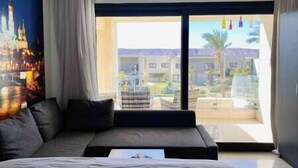 Et moderne hotelværelse med en stor seng, en mørk sofa og udsigt til en pool og bygninger gennem den store skydedør.