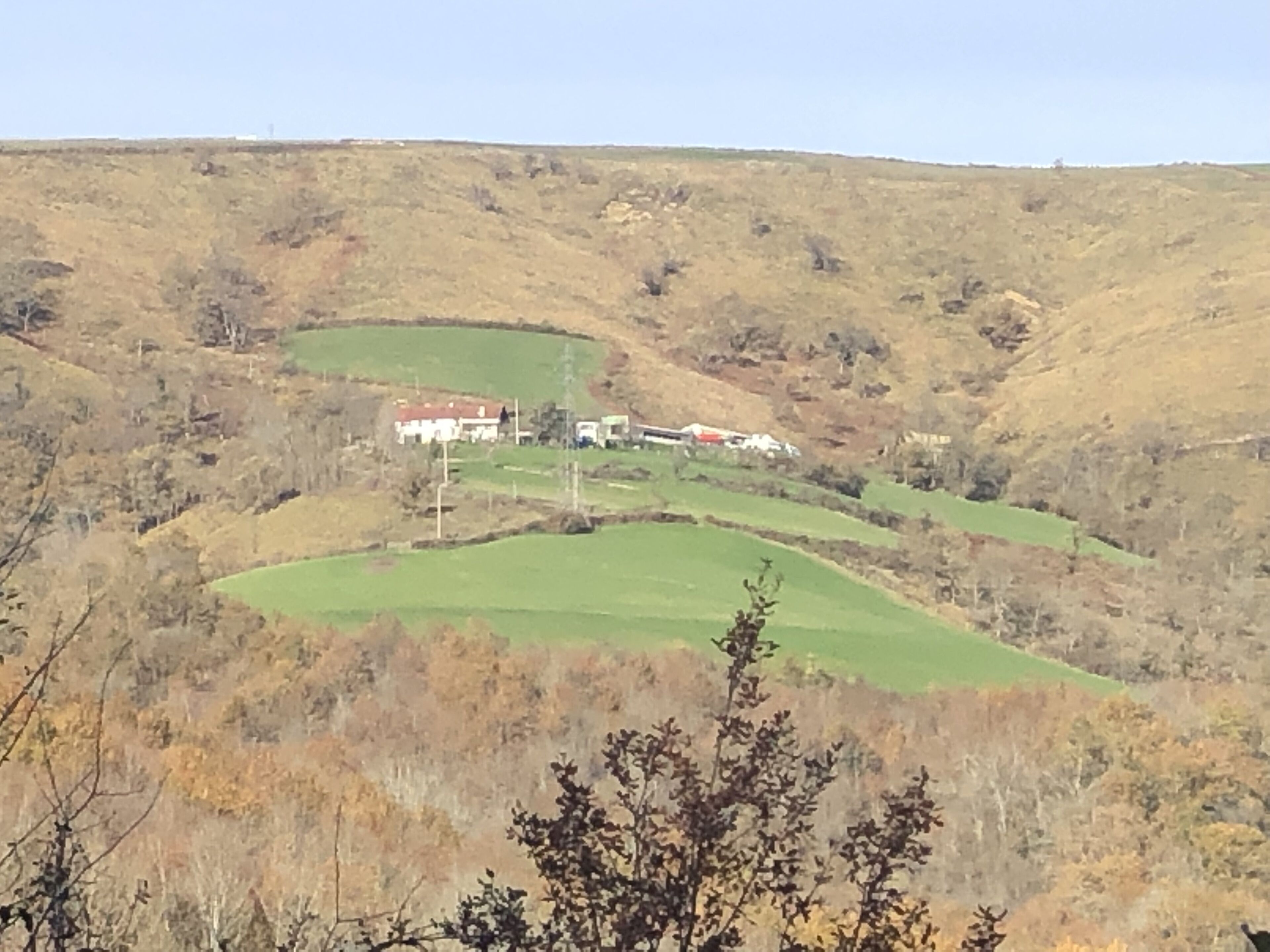 A rural landscape with rolling hills, a few buildings, and sparse vegetation.