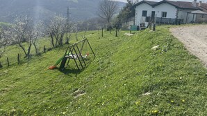 A grassy area with a swing set and a white building with a red roof. - Gite Lasterenborda (Osses)