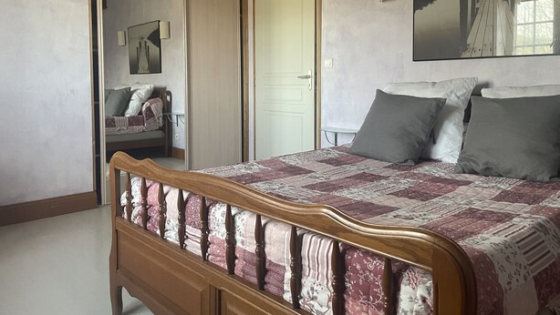 A bedroom with a wooden bed, a white door, a small table, and a chair. - Gite Lasterenborda (Osses)