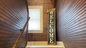 Een houten trap met een 'WELCOME' bord, een raam en een houten leuning.