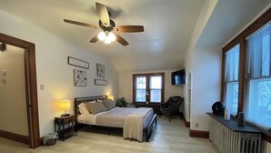 Een slaapkamer met een bed, een plafondventilator, een radiator en een televisie aan de muur.