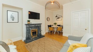 Una sala de estar con chimenea, comedor con mesa y sillas, televisor montado en la pared y una puerta.
