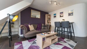 A modern living room with a sofa, coffee table, and two bar stools. - Perth Penthouse at the Concert Hall (Perth and Kinross)