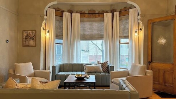 A cozy living room with a sofa set, a coffee table, and a window with curtains. - Epic 8BR Milwaukee Victorian House (Milwaukee)