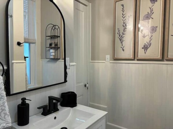A bathroom with a white vanity, a black soap dispenser, a black towel, and a mirror with a black frame. There are framed floral pictures on the wall.