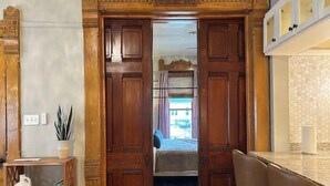 A room with a wooden door leading to a balcony, a small table with a vase and books, and a chair. - Epic 8BR Milwaukee Victorian House (Milwaukee)