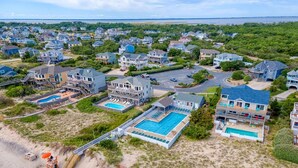 An aerial view of a coastal residential area with houses, a beach, and a large swimming pool complex. - Oceanside vacation rental steps away from the beach access in Corolla, NC! (Corolla)