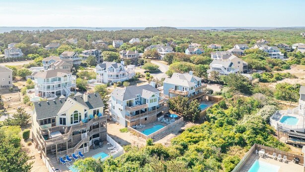 A residential area with multiple houses, a large swimming pool, and a view of the ocean. - Oceanside vacation rental steps away from the beach access in Corolla, NC! (Corolla)