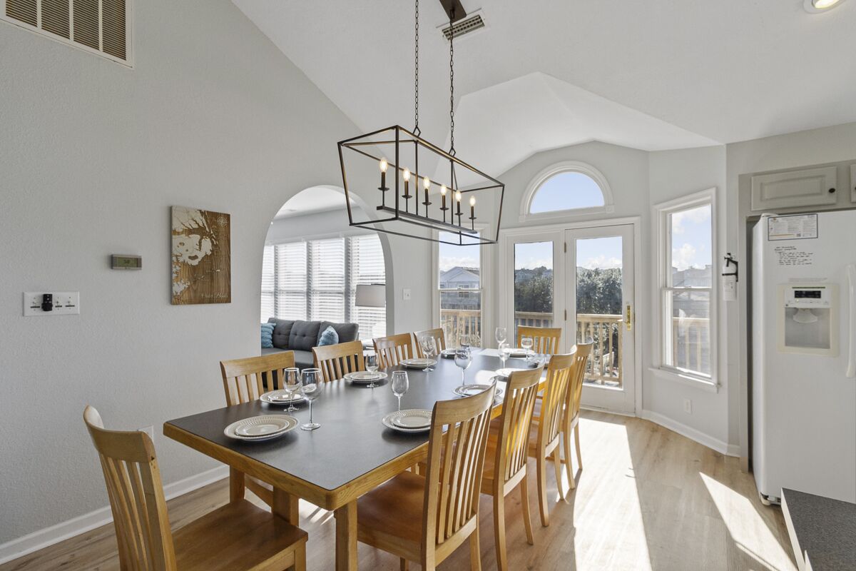 A dining area with a wooden table set for six, surrounded by wooden chairs.