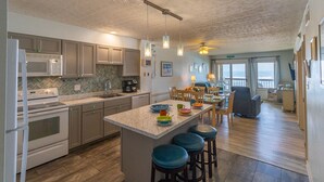 A modern kitchen with a central island, bar stools, and a dining area with a view. - Beautiful sunrise views from this oceanfront condo in Kill Devil Hills NC! (Kill Devil Hills)